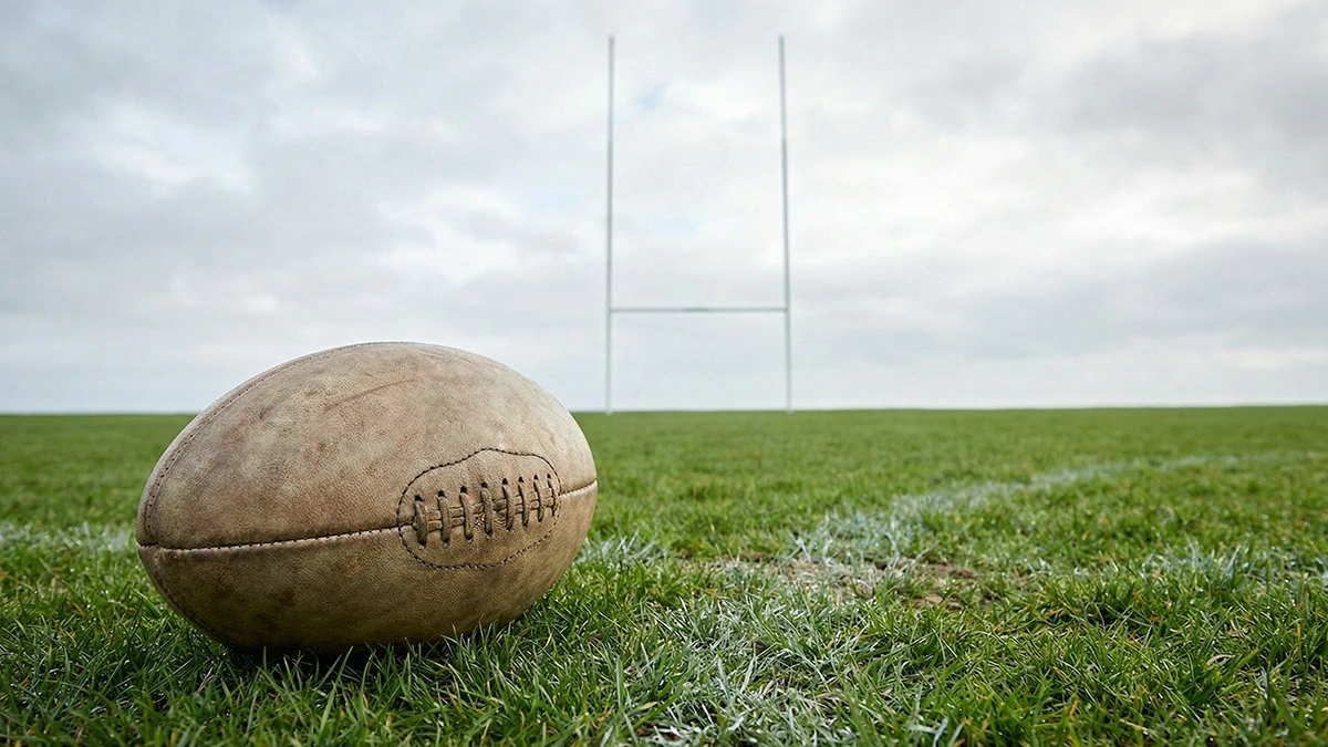 Ballon de rugby ovale posé sur une pelouse de stade avec les poteaux de but en arrière-plan